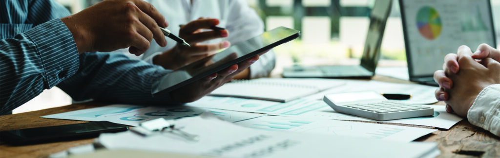 Multiple people working on paperwork, charts, and graphs with smartphones and computers